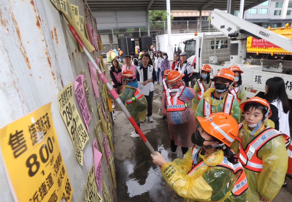 《圖說》清潔隊員的日常工作不僅要道路清掃和垃圾收運,其中包括刮除小廣告。小局長體驗拿起刮刀刮除路邊惱人的小廣告。〈環保局提供〉